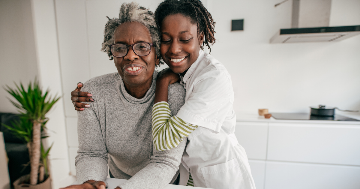 A smiling caregiver embraces a senior woman at home, reflecting trust, companionship, and compassionate in-home care support.