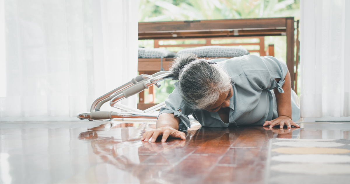 An elderly woman lying on the floor near a fallen walker after losing balance at home, illustrating fall risk and the need for home care assistance.