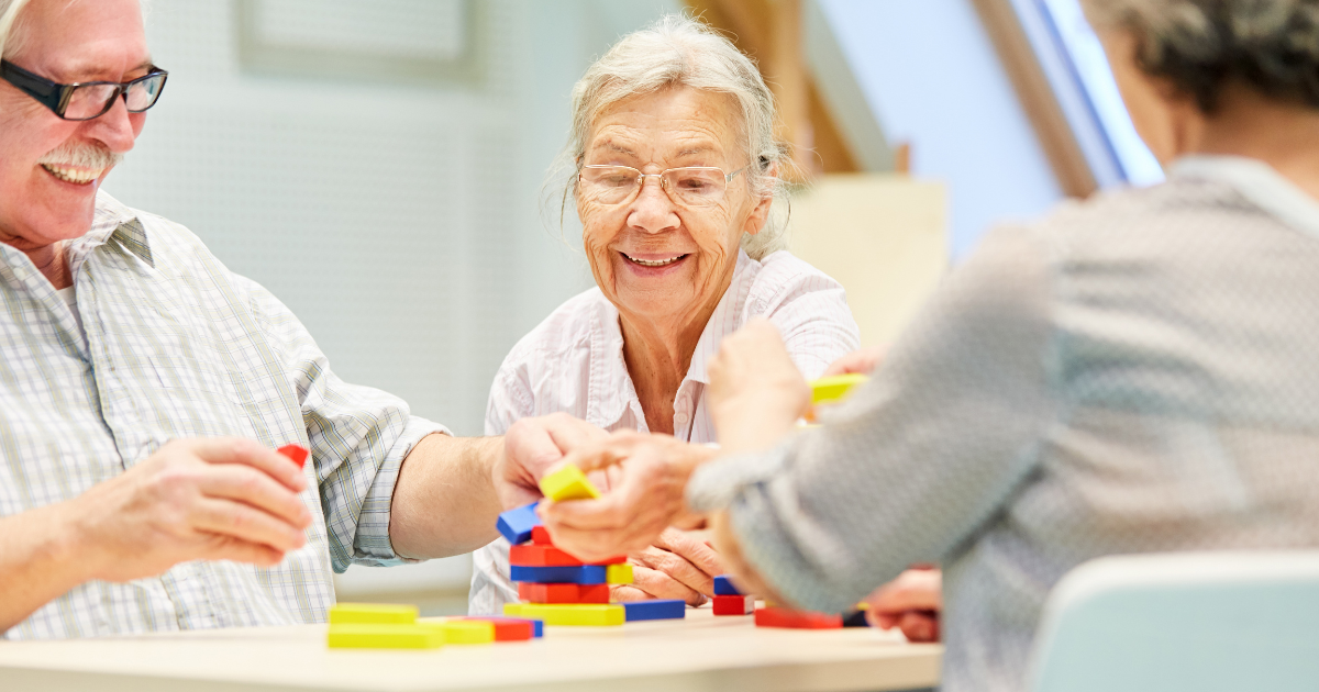 Seniors smiling and playing a colorful tabletop game together, promoting cognitive stimulation, social interaction, and mental wellness.