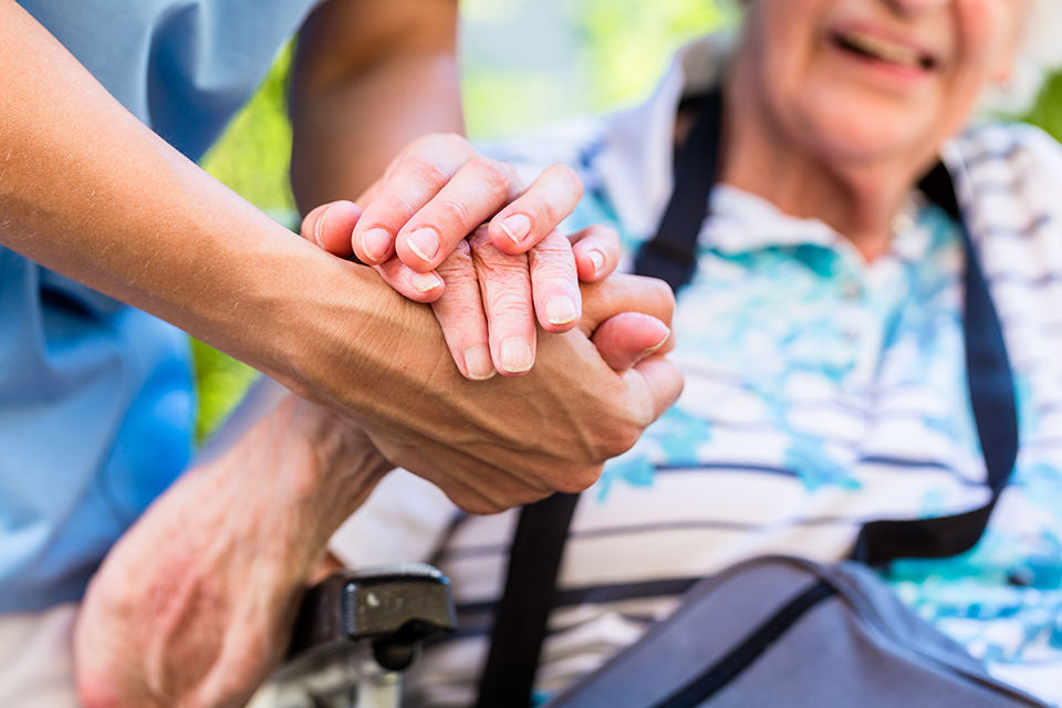 Compassionate Senior Home Care Support A caregiver gently holding the hand of a smiling elderly woman in a supportive and caring gesture.